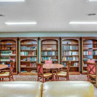 A cozy library reading area with wooden bookshelves, tables, and chairs.