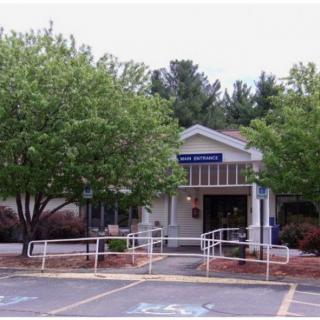 A small library building surrounded by trees with a parking area in front.