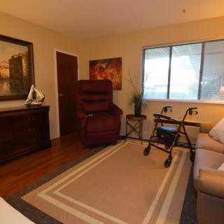 A cozy living room with a recliner, sofa, and a walker by the window.