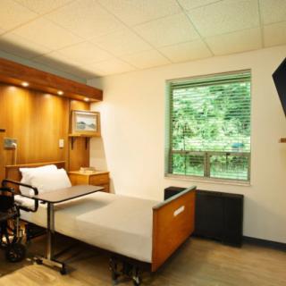 A hospital room with a patient bed, wheelchair, and a window with a view of the outdoors.