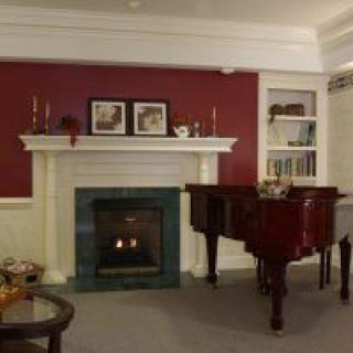 A cozy living room featuring a red accent wall, a white mantelpiece with a fireplace, and a glossy grand piano.
