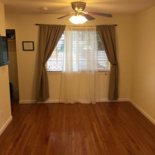 A cozy living room with hardwood floors and a ceiling fan, featuring a window adorned with curtains.