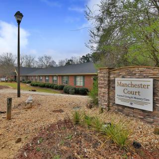 A view of an apartment complex with a sign reading 'Manchester Court' and a landscaped pathway.