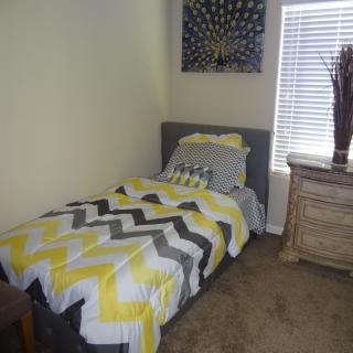 A cozy bedroom with a single bed featuring a zigzag-patterned comforter next to a wooden nightstand.