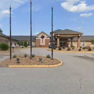 A view of a building entrance with a driveway and landscaping under a partly cloudy sky.