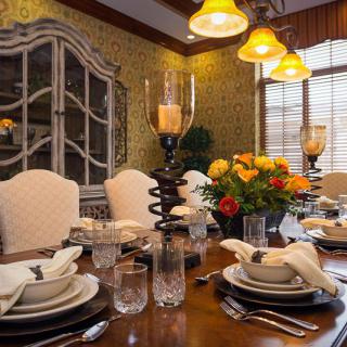 An elegantly set dining table with candles and floral centerpiece, surrounded by plush chairs and warm lighting.