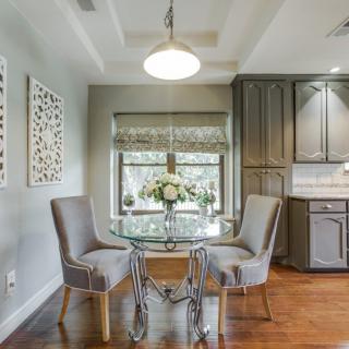 A modern dining area with a glass table and elegant chairs, featuring sleek cabinetry and a hardwood floor.