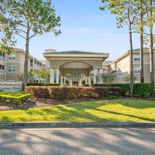 The entrance of a residential building surrounded by trees and well-kept landscaping on a sunny day.