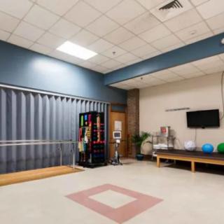 A spacious exercise room with therapy equipment and a TV screen.