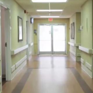 A long, empty hospital corridor with green walls and bright lighting.