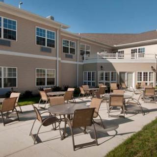 A sunny outdoor patio area with tables and chairs in front of a residential building.