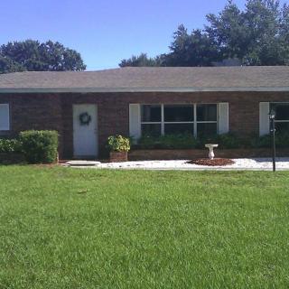 A single-story brick house with a maintained front lawn and surrounding trees.