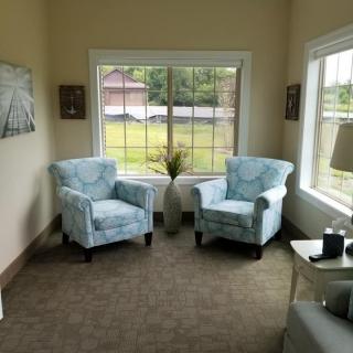 A cozy living room with two patterned armchairs positioned near large windows, offering a view of the outside.