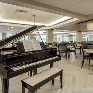 A spacious interior room featuring a grand piano and several tables and chairs, ideal for events or gatherings.