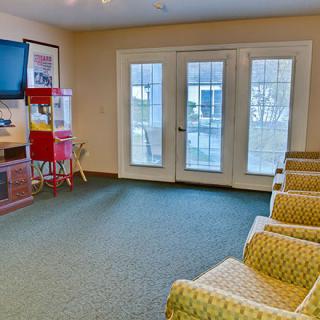 A cozy waiting room with comfortable chairs, a television, and a popcorn machine beside glass doors.