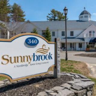 A sign for Sunnybrook, a retirement living community, stands in front of a large building.