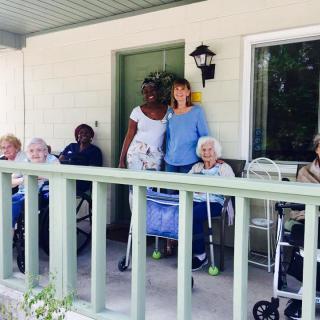 A group of elderly people and caregivers sitting on a porch enjoying the outdoors.