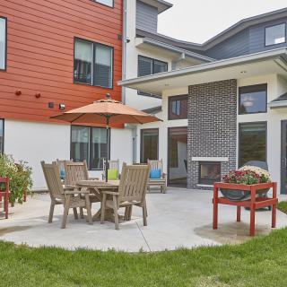 A cozy outdoor patio area with a table, chairs, and a large umbrella outside a modern building.