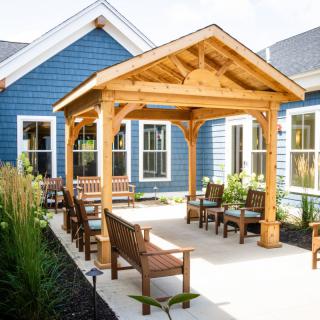 A charming patio area with a wooden pergola, surrounded by blue house exteriors and outdoor seating.