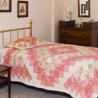 A traditional bedroom with a single bed covered by a patterned quilt.