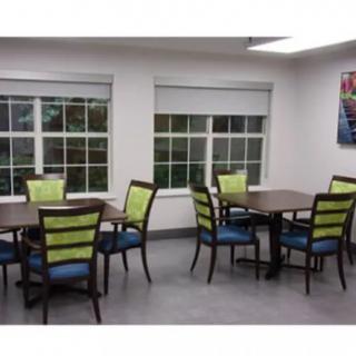 A well-lit dining area with chairs and tables, featuring large windows.