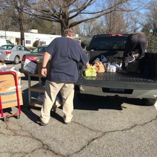 A man loading grocery items into the back of a pickup truck in a parking area.