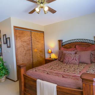 A cozy bedroom with a wooden bed, warm-toned bedding, and a ceiling fan.
