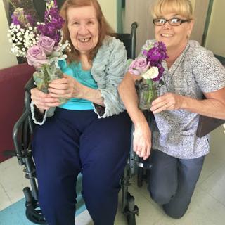 A joyful moment shared between a resident and a caregiver, both holding lovely bouquets of flowers.