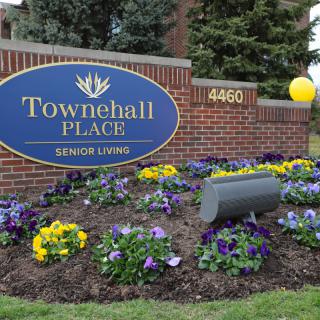 A sign for Townehall Place Senior Living surrounded by colorful flowers and a small balloon tied to the signpost.