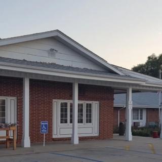 A brick building with a covered porch and adjacent parking area in the early evening light.