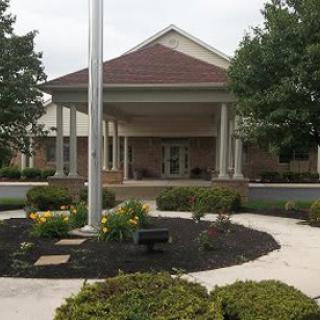 A building entrance with a covered porch, surrounded by neatly arranged landscaping and a flagpole.