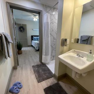 A modern bathroom featuring a shower, sink, and a view of the adjoining bedroom.
