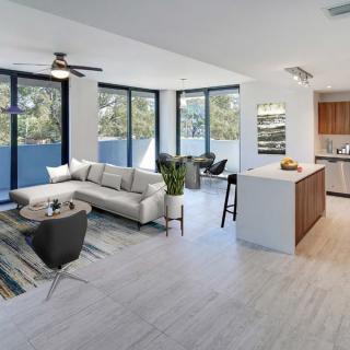 A modern open floor plan living room with a kitchen, featuring large windows and contemporary furnishings.