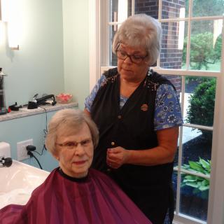 A hairstylist is giving a haircut to an elderly woman in a salon.