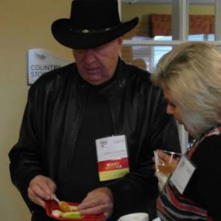 Two individuals at a social gathering, one wearing a cowboy hat and holding food.