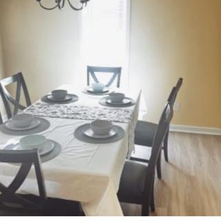 A dining room with a neatly set table, featuring a white tablecloth, black chairs, and matching dishware.