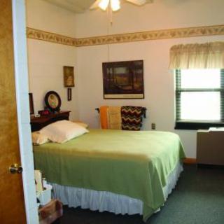 A cozy bedroom featuring a neatly made bed with green bedding, wall art, and a window with drapes.