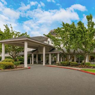 A large building with a columned entrance and surrounding greenery under a partly cloudy sky.