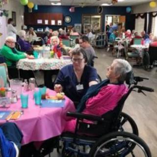 A caregiver interacting with residents at a nursing home during a communal gathering.