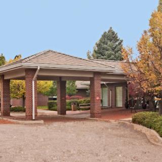 A brick structure with an overhang and a circular driveway, surrounded by landscaped greenery.