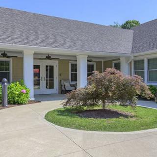 A welcoming entrance to a residential building with landscaped greenery and a curved sidewalk.