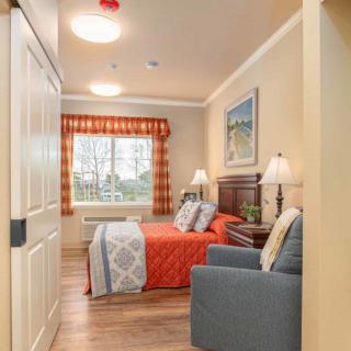 A cozy bedroom featuring a bed with red bedding, two bedside lamps, and a window with patterned curtains.