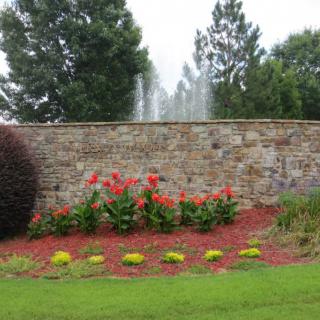 A beautifully landscaped garden with vibrant flowers in front of a stone wall and fountain.