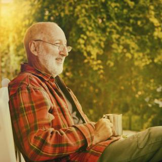 An elderly man enjoys a peaceful moment outdoors with a cup of coffee.