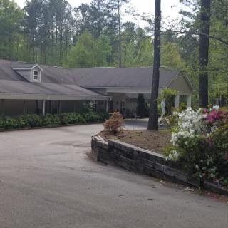 A house with a driveway surrounded by trees and flowers in a landscaped garden.
