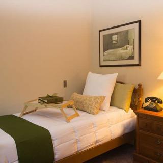 A cozy bedroom with a single bed featuring green accents, a nightstand with a lamp, and a decorative tray.