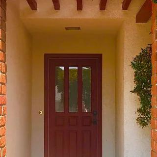 A cozy entrance featuring a red front door surrounded by brick walls, with wooden beams overhead and greenery to the side.