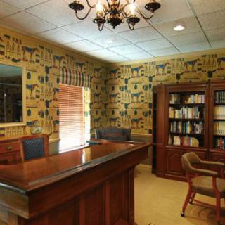 Cozy office interior with a wooden desk, bookshelves, and patterned wallpaper.