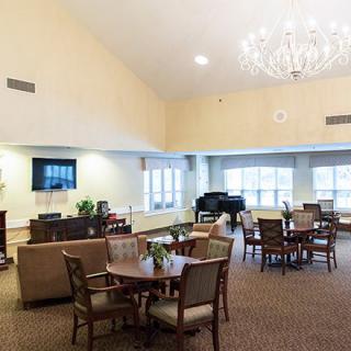 A spacious living room with elegant furniture, a chandelier, and a piano near large windows.