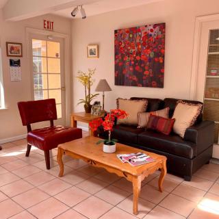 A cozy living room with a sofa, red chair, and wooden coffee table, adorned with plants and artwork on the wall.